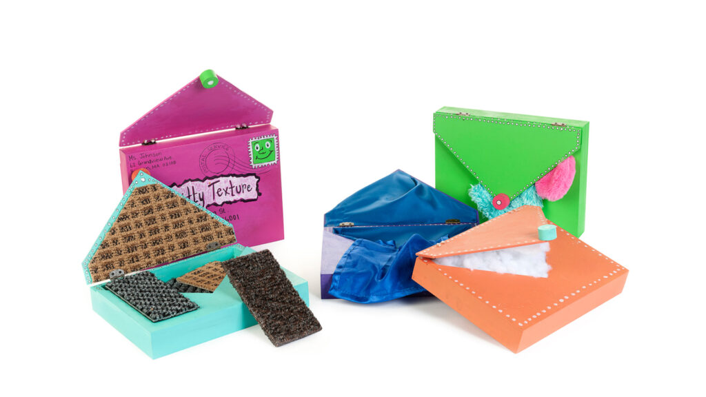Three artistic renditions of envelopes on a white background, each open to reveal different tactile textures or contents. The pink envelope on the left has a green frog stamp and contains various textured squares. The green envelope in the middle contains blue fabric. The orange envelope on the right is filled with white fluffy material.