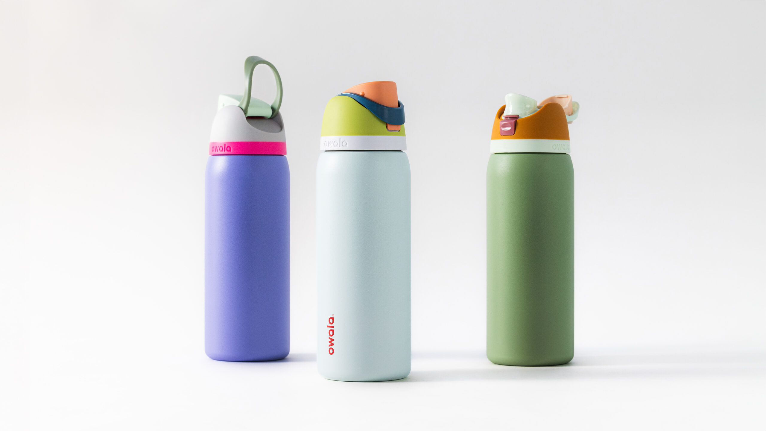 Three colorful Owala water bottles stand upright on a white background. Each bottle features a different combination of bright, contrasting colors and a flip-top lid with a built-in straw.