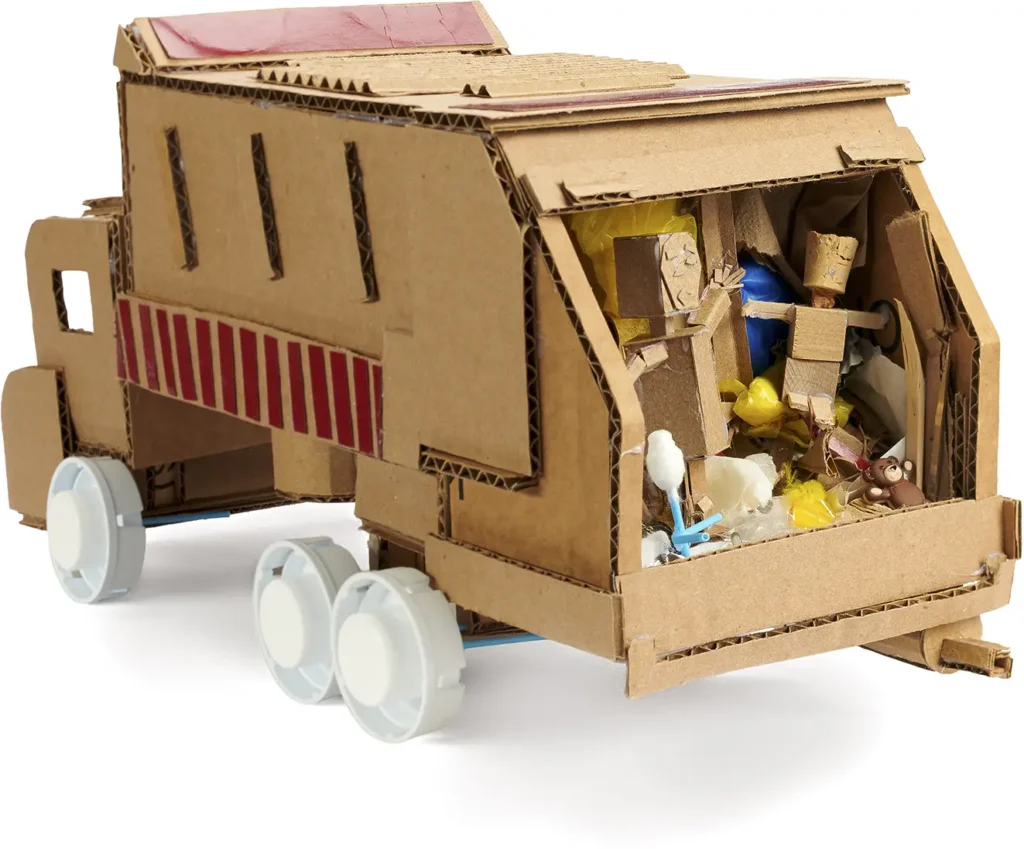 A handmade model truck constructed from cardboard and recycled materials, with bottle cap wheels and a bed filled with small figures and craft supplies.